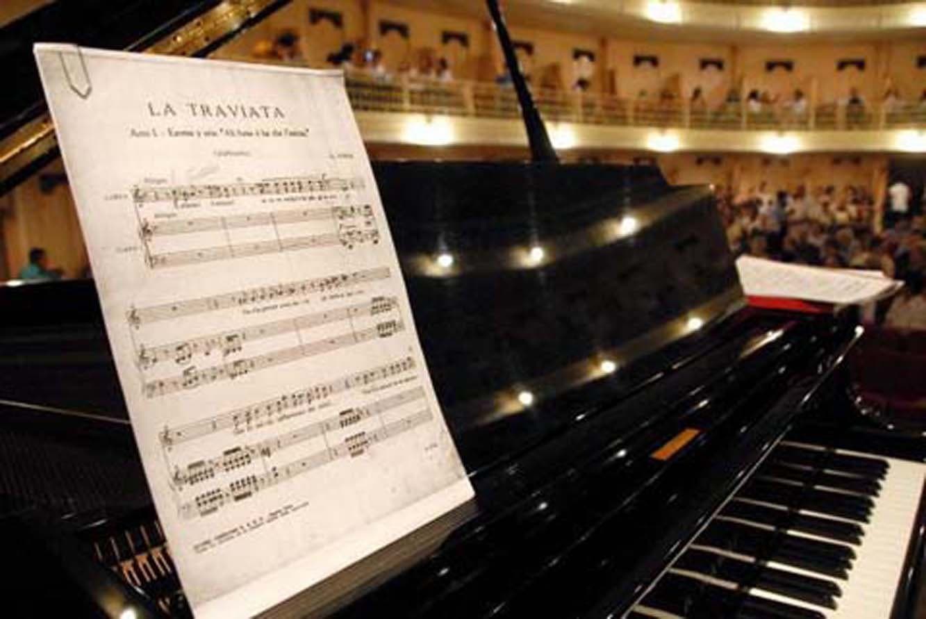 A partitura de “La Traviata” ao piano, com a sala cheia ao fundo.