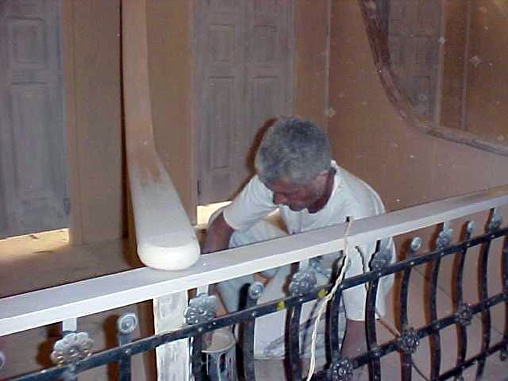 Um pintor trabalha no parapeito de um camarote, junto ao gradil de ferro.