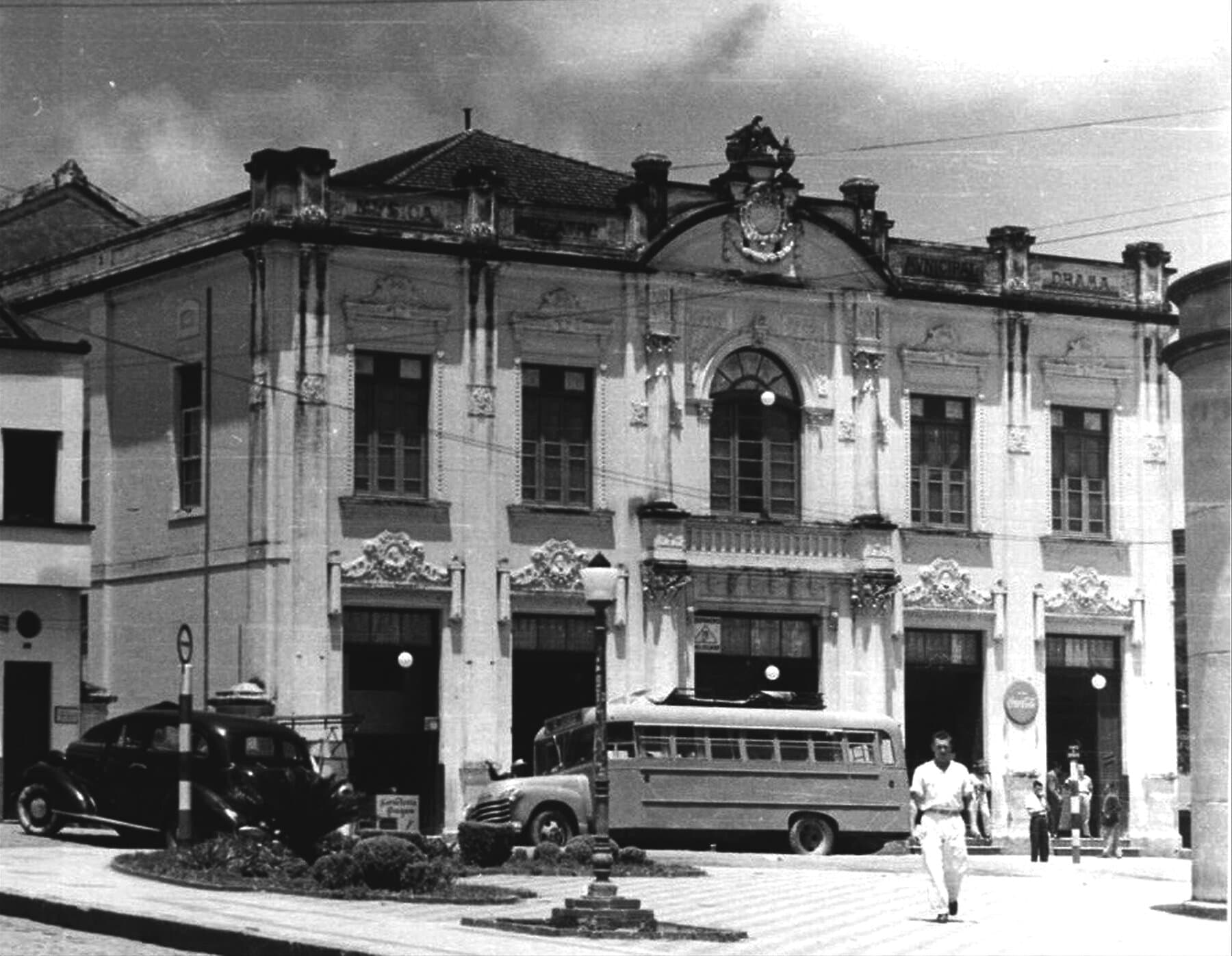 A fachada eclética do Theatro Municipal, com as inscrições ligadas à música e ao drama, diante da praça do centro.
