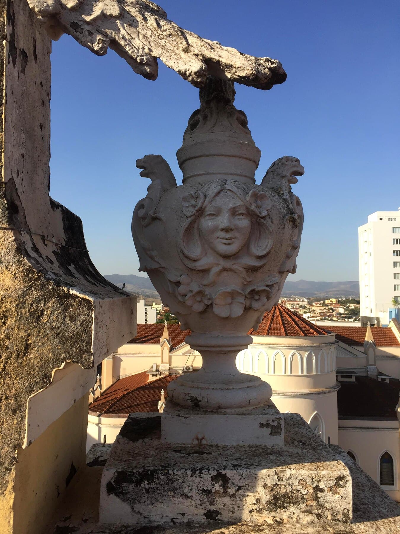 Acrotério da platibanda — urna ornamental com ave, restaurada e recortada contra o céu.