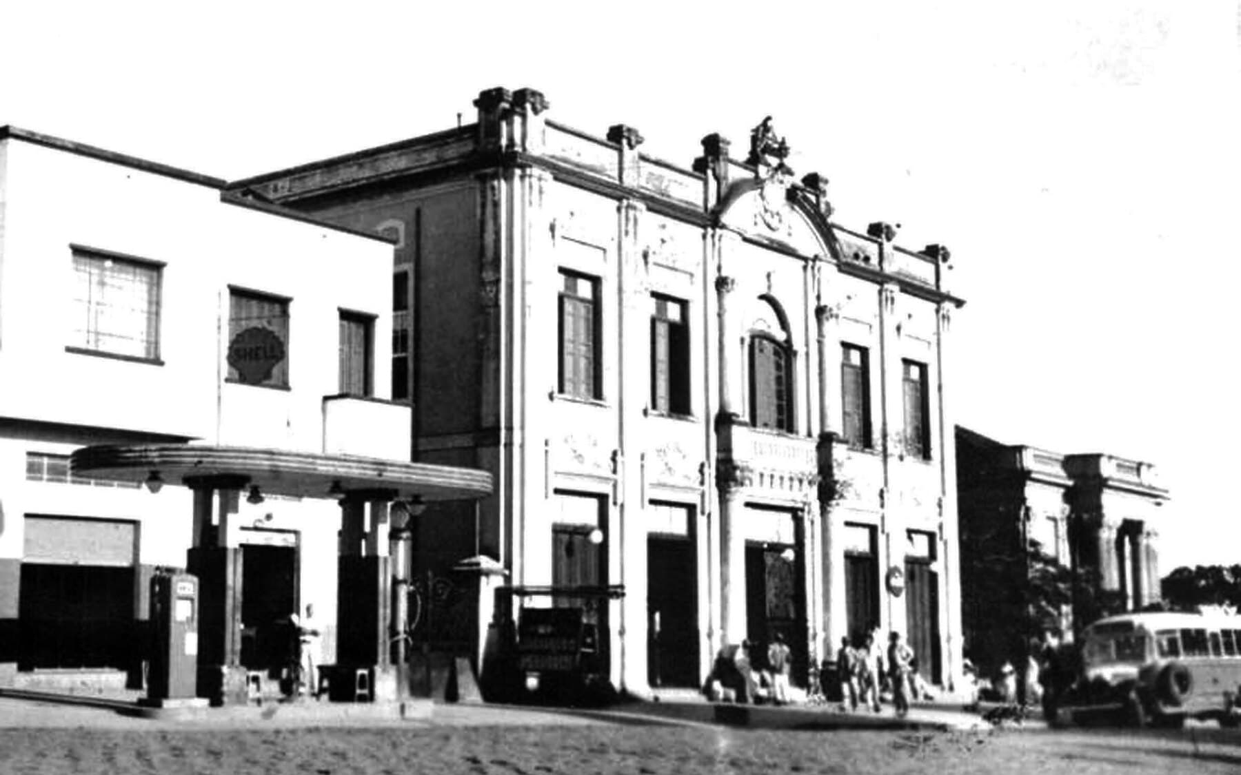O Theatro e o movimento da rua, com automóveis de época, em registro antigo.
